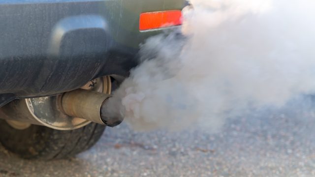 Thick smoke pours from the exhaust pile on a car. Shallow depth of field, focus on the end of the tail pipe. Closeup view.