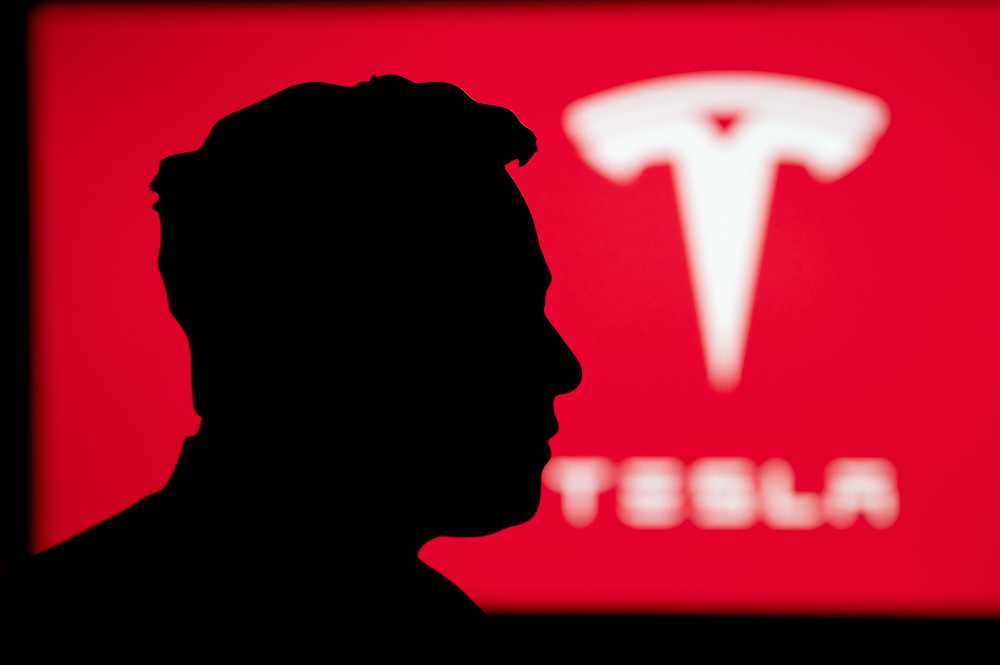 Silhouette of Elon Musk portrait, billboard of Tesla on red background — Photo by kovop58@gmail.com