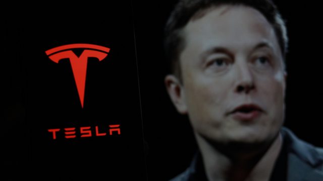Tesla logo is displayed on smartphone screen With CEO Elon Musk in a background. — Photo by MuhammadAlimaki