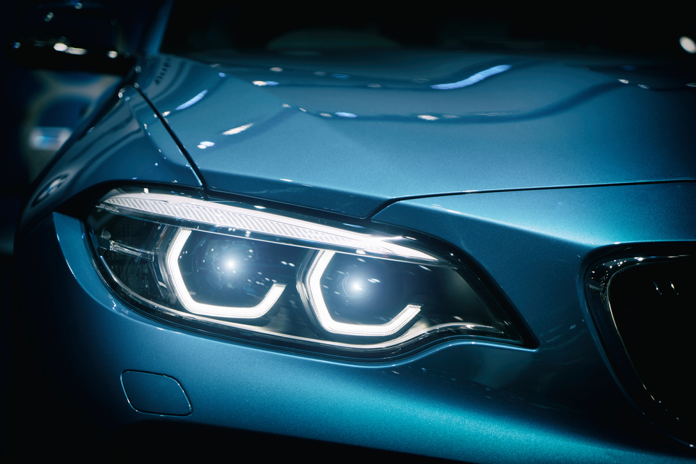 Car headlight and hood of powerful sports blue car with blue glare on dark background. Close up at Car headlight.