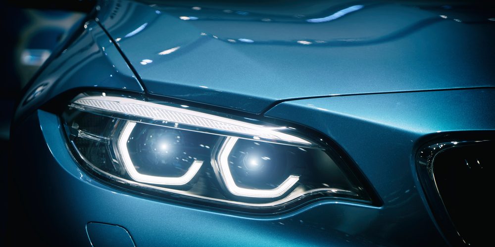 Car headlight and hood of powerful sports blue car with blue glare on dark background. Close up at Car headlight.