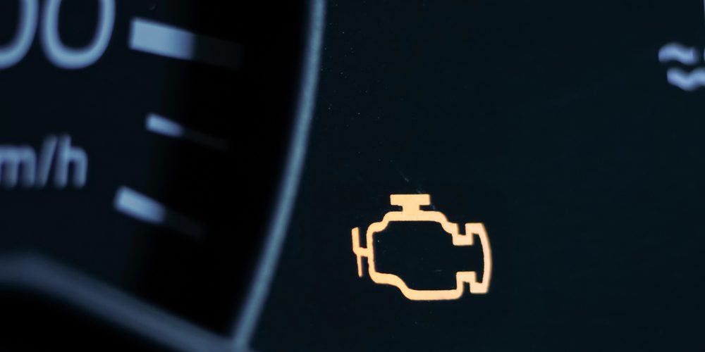 Yellow lit engine error sign on car dashboard close up