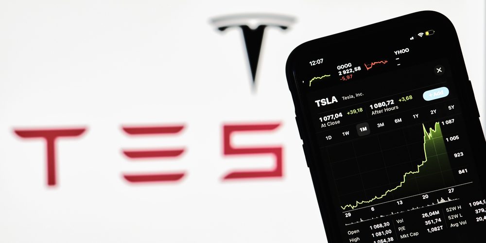 Tesla stock share growth Tesla stock share growth. Hand holds a mobile phone with growing Tesla shares graph on stock market over Tesla logo on background (image courtesy Deposit Photos)