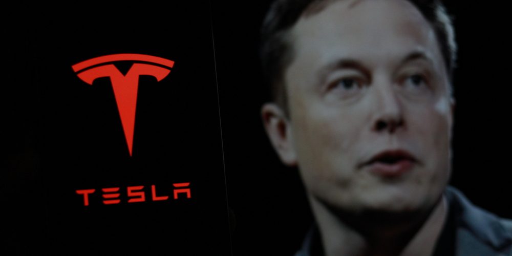 Tesla logo is displayed on smartphone screen With CEO Elon Musk in a background. — Photo by MuhammadAlimaki