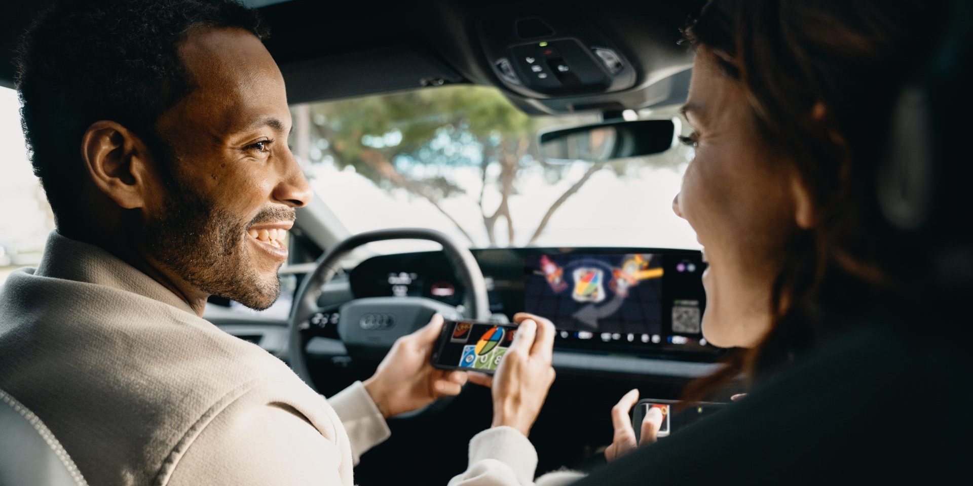 Gaming fun on the go: Audi integrates AirConsole A game from the AirConsole gaming platform runs on the touch display in an Audi. The driver and passenger smile at each other and each hold a smartphone in their hands. They use the smartphones as controllers to play the games (image courtesy Audi)