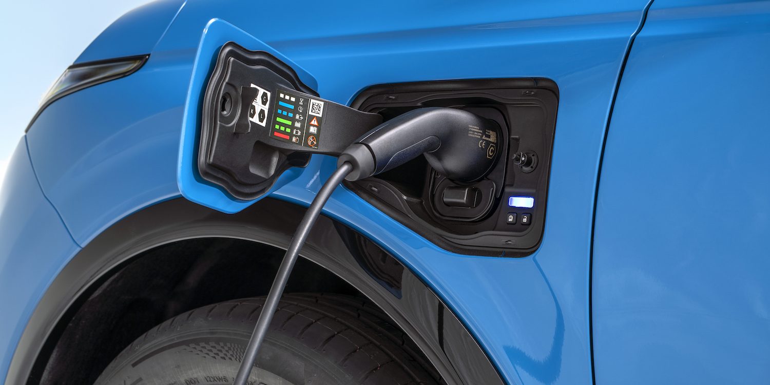 detailed shot of open electric charging port with a charger plugged in on left side above the wheels detailed shot of open electric charging port with a charger plugged in on left side above the wheels